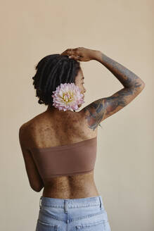 Young woman with short hair holding peony flower against brown background - KPEF00266