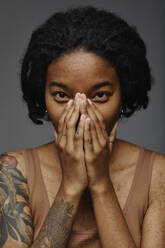 Young woman covering face with hands against gray background - KPEF00281