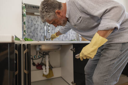 Älterer Mann repariert Wasserhahn in der Küche zu Hause - JCCMF10736