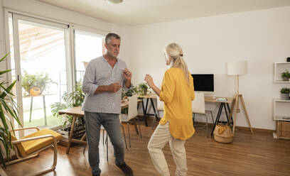 Carefree couple dancing together in living room at home - JCCMF10748