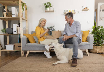 Mann überrascht Frau mit Geschenk auf Sofa sitzend bei Hund zu Hause - JCCMF10751