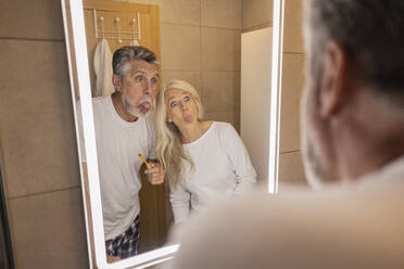 Man and woman sticking out tongue looking in mirror at home - JCCMF10765