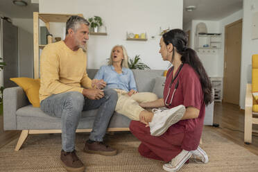 Pflegekraft untersucht eine Frau, die mit einem Mann auf dem Sofa zu Hause sitzt - JCCMF10779