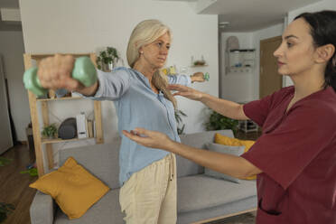 Pflegekraft hilft einer Frau bei Übungen mit Hanteln zu Hause - JCCMF10785