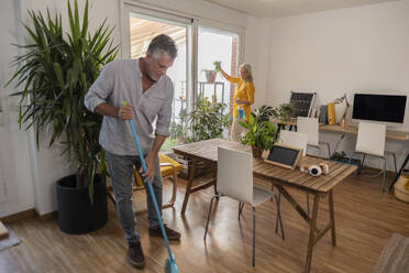 Mann und Frau beim Reinigen des Wohnzimmers zu Hause - JCCMF10806