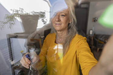 Reife Frau putzt Fensterglas - JCCMF10808