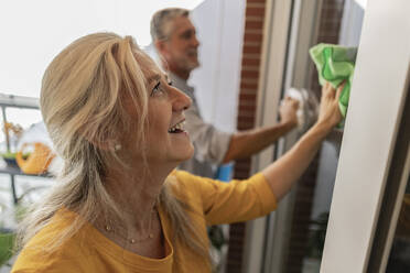 Happy woman cleaning house window - JCCMF10811