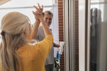 Happy couple giving high-five standing near window - JCCMF10813