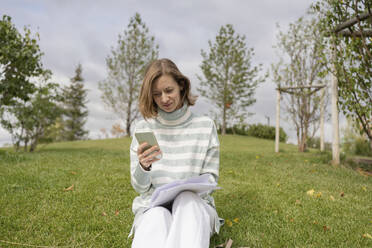 Frau sitzt im Gras und benutzt ihr Smartphone im Park - LESF00480