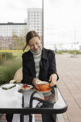 Lächelnde Frau mit Teetasse in einem Straßencafé - LESF00485