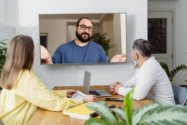 Kollegen kommunizieren mit Geschäftsmann per Videoanruf über TV im Büro - OSF02177