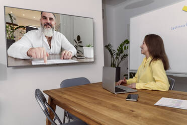 Geschäftsfrau, die mit einem Kollegen per Videogespräch über einen Fernseher im Besprechungsraum eine Strategie plant - OSF02179