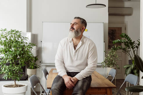 Businessman sitting with eyes closed on table at work place - OSF02181