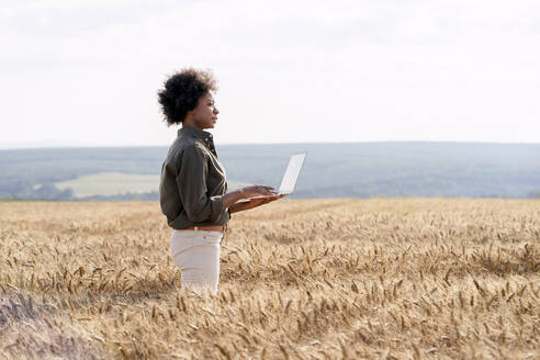 Afro-Bauer mit Laptop inmitten von Gerstenkulturen auf dem Feld - AAZF01155