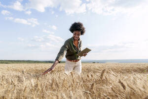 Lächelnder junger Afro-Agronom mit Tablet-PC bei der Untersuchung von Gerste auf einem Feld - AAZF01175