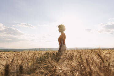 Young woman enjoying solitude in barley field at sunset - AAZF01186