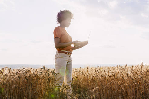 Junger Afro-Agronom mit Laptop im Gerstenfeld - AAZF01190