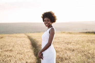 Glückliche junge Frau in einem Weizenfeld bei Sonnenuntergang - AAZF01224