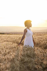 Junge Frau in weißem Kleid steht in einem Weizenfeld bei Sonnenuntergang - AAZF01228
