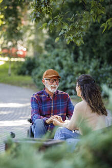 Smiling retired senior man in wheelchair holding hands with caregiver - IKF01316