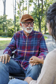 Smiling retired senior man in wheelchair looking at caregiver - IKF01319