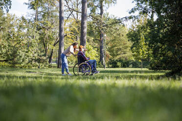 Social worker gesturing to senior man in wheelchair at park - IKF01327