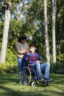Smiling senior man in wheelchair looking at volunteer in park - IKF01328