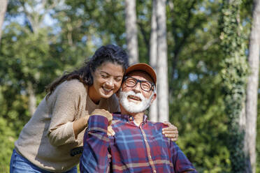 Smiling caregiver embracing retired senior man at park - IKF01329