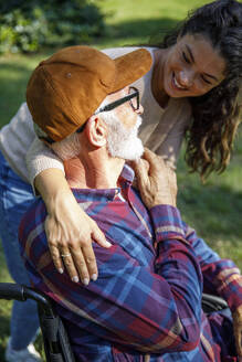 Smiling volunteer with hands on retired senior man's shoulders at park - IKF01332