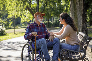 Happy retired senior man in wheelchair talking with volunteer - IKF01346