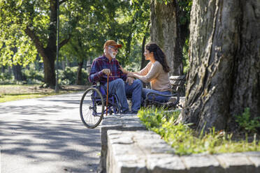 Happy retired senior man in wheelchair talking with volunteer at park - IKF01348