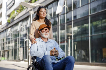 Smiling social worker behind senior man in wheelchair - IKF01364