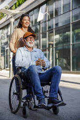 Smiling caregiver behind senior man in wheelchair - IKF01365