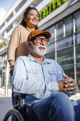 Smiling volunteer behind senior man in wheelchair - IKF01366
