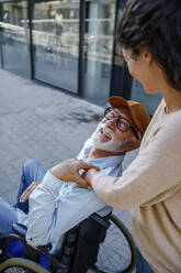 Happy senior man in wheelchair looking at caregiver - IKF01369