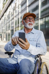 Retired senior man using smart phone sitting in wheelchair - IKF01378