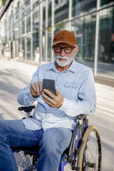 Retired senior man sitting in wheelchair using mobile phone - IKF01379