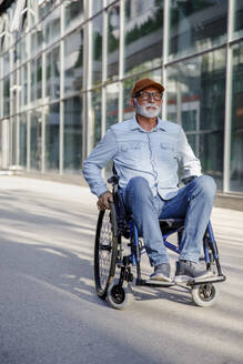 Retired senior man sitting in wheelchair on footpath - IKF01380