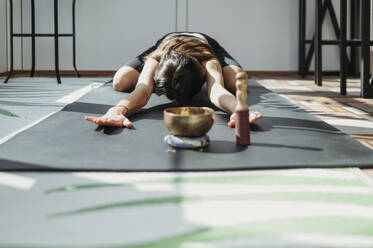 Frau übt Balasana-Pose auf Yogamatte zu Hause - ANAF02175