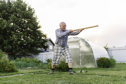 Älterer Mann spielt mit Holzstab im Garten - EYAF02838