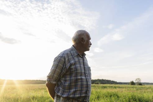 Älterer Mann steht bei Sonnenuntergang auf einem Feld - EYAF02842