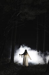 Ghost with knife standing in front of smoke in forest at night - MASF39557