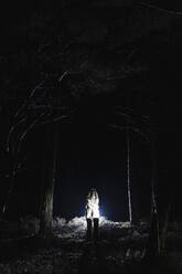 Spooky female ghost standing amidst trees in forest at night - MASF39562