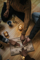 Hohe Winkel Ansicht der multirassischen Freunde mit Ouija Board sitzen auf Hartholzboden - MASF39574