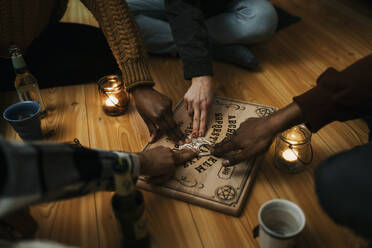 Multirassische männliche und weibliche Freunde benutzen Ouija-Brett im Haus - MASF39576