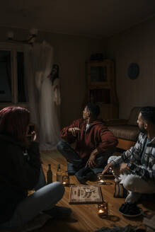 Verängstigte multirassische Freunde mit Ouija-Brett, die einen Geist in einer Hütte sehen - MASF39589