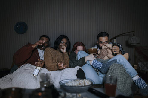 Verschiedenste Freunde genießen gemeinsam einen Horrorfilm auf dem Sofa in einer gemütlichen Hütte - MASF39590