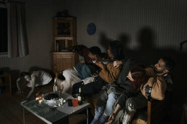 Verängstigte gemischtrassige Freunde, die einen gruseligen Geist betrachten, während sie einen Gruselfilm in einer Hütte ansehen - MASF39596