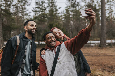Fröhliche Freunde unterschiedlicher Herkunft machen im Hof ein Selfie mit dem Smartphone und strahlen dabei - MASF39624