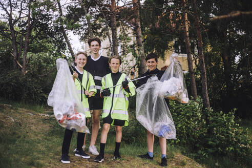 Full length portrait of smiling boys standing with plastic bags - MASF39629